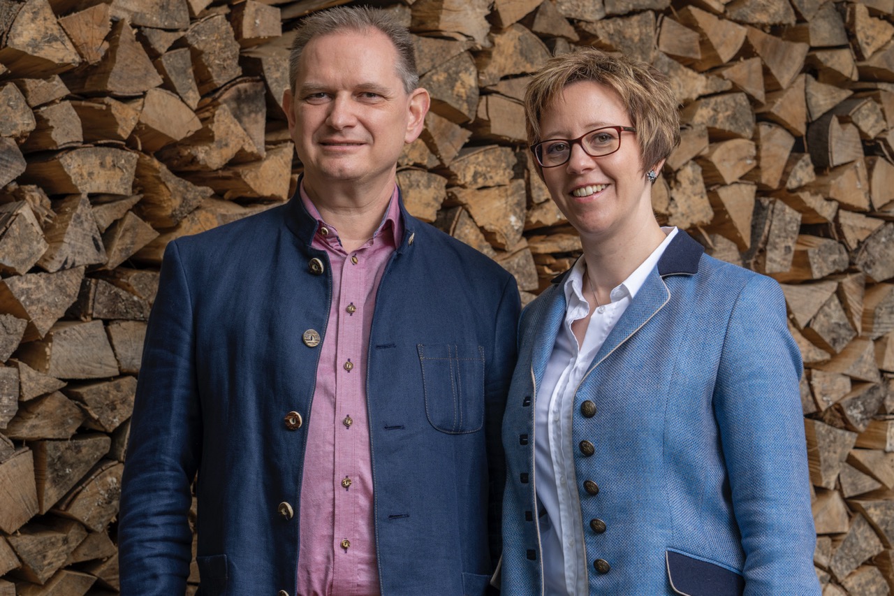 Claudia und Daniel Bürki stehend vor Holzhintergrund gekleidet in Trachtenmode mit Bluse, Hemd und Janker. Eine grosse Auswahl an Trachtenmode wie Janker, Westen, Hemden, Blusen, Dirndl, Lederhosen findest Du bei Musik und Mode Bürki in Fehraltorf im Zürcher Oberland in der Schweiz.