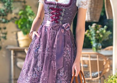 Frau in Midi-Dirndl in Violett mit Dirndlbluse aus Spitze. Eine grosse Auswahl an Dirndlblusen und Dirndl der Marke MarJo und Krüger findest du bei Musik und Mode Bürki in Fehraltorf im Zürcher Oberland.